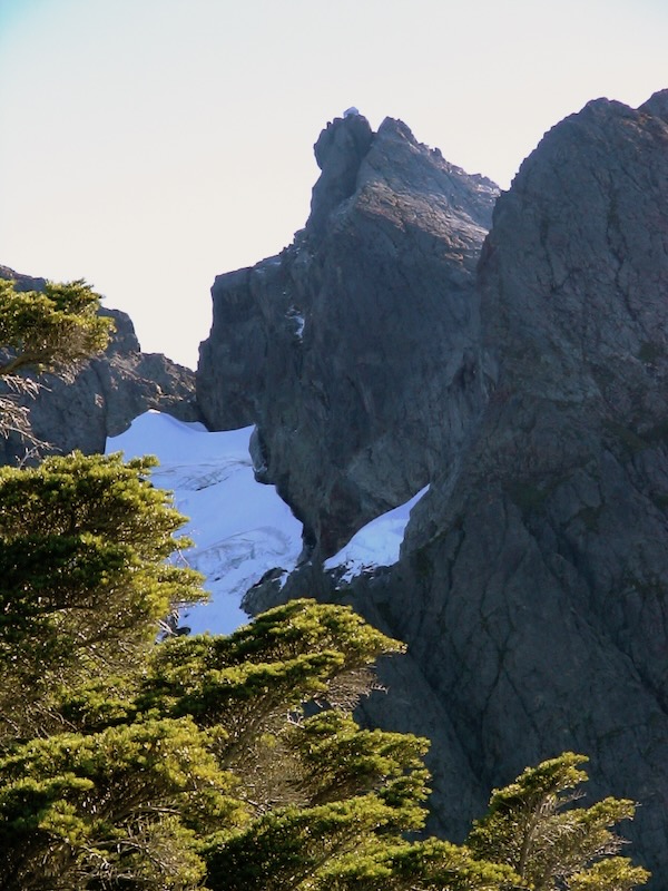 forground trees, snow banks, cabin on isolated peak
